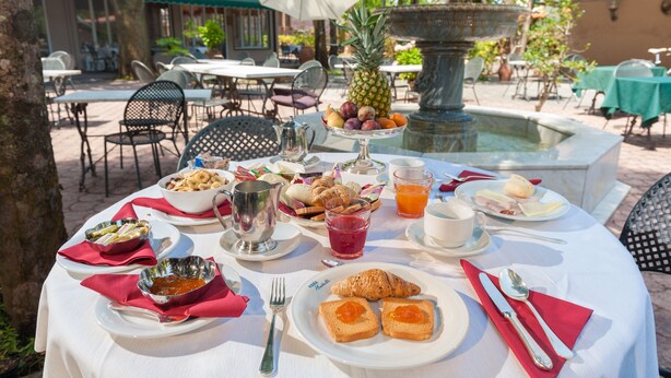 An outdoor dining area with a table set for breakfast, including bread, fruit, and beverages. - Albergo Battelli - Adults Only  (Pietrasanta)
