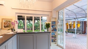 A reception area with a counter, framed artwork, and a window with a view of greenery. - Albergo Battelli - Adults Only  (Pietrasanta)