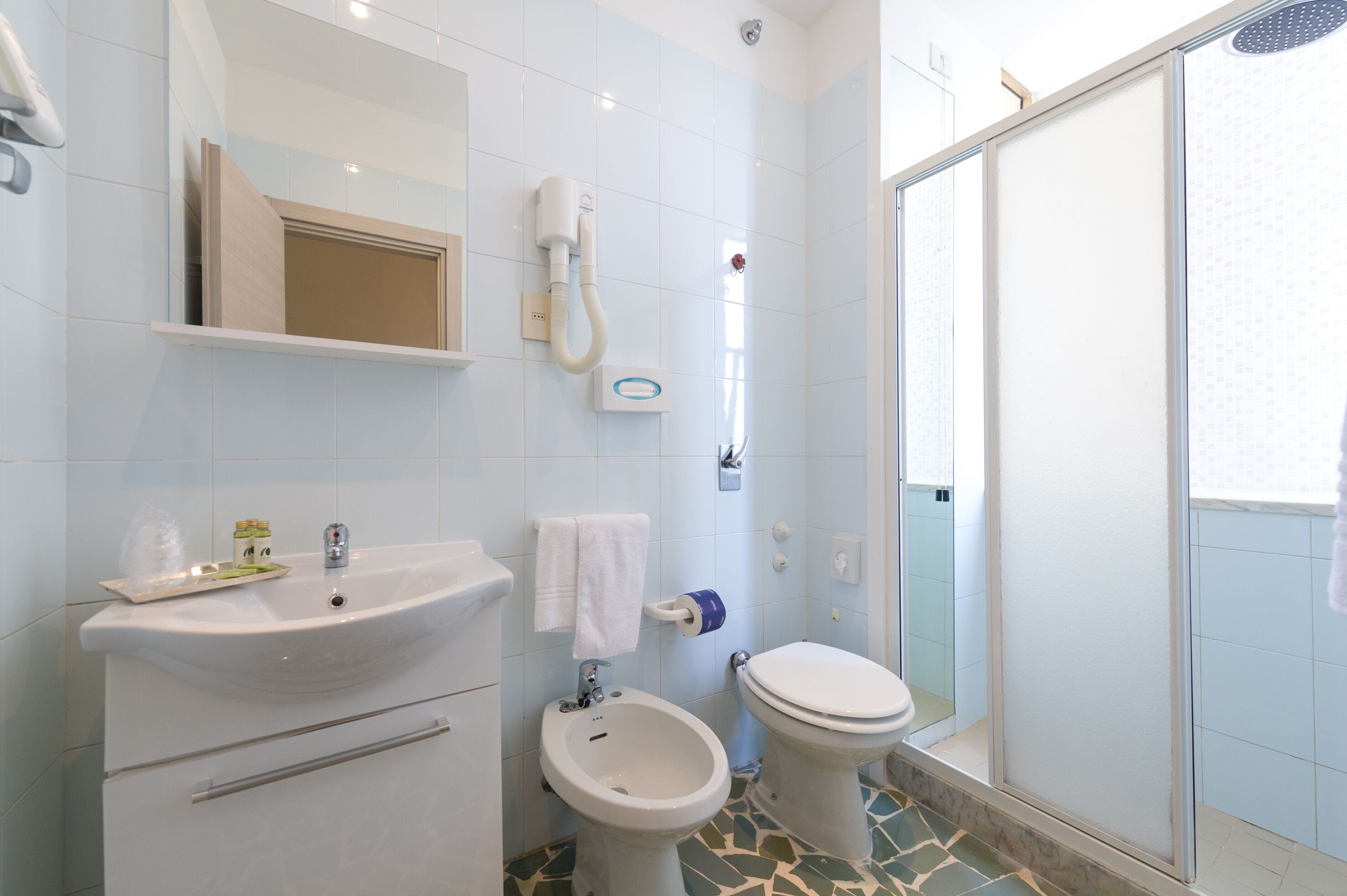 A bathroom with a sink, bidet, toilet, and a shower enclosure.