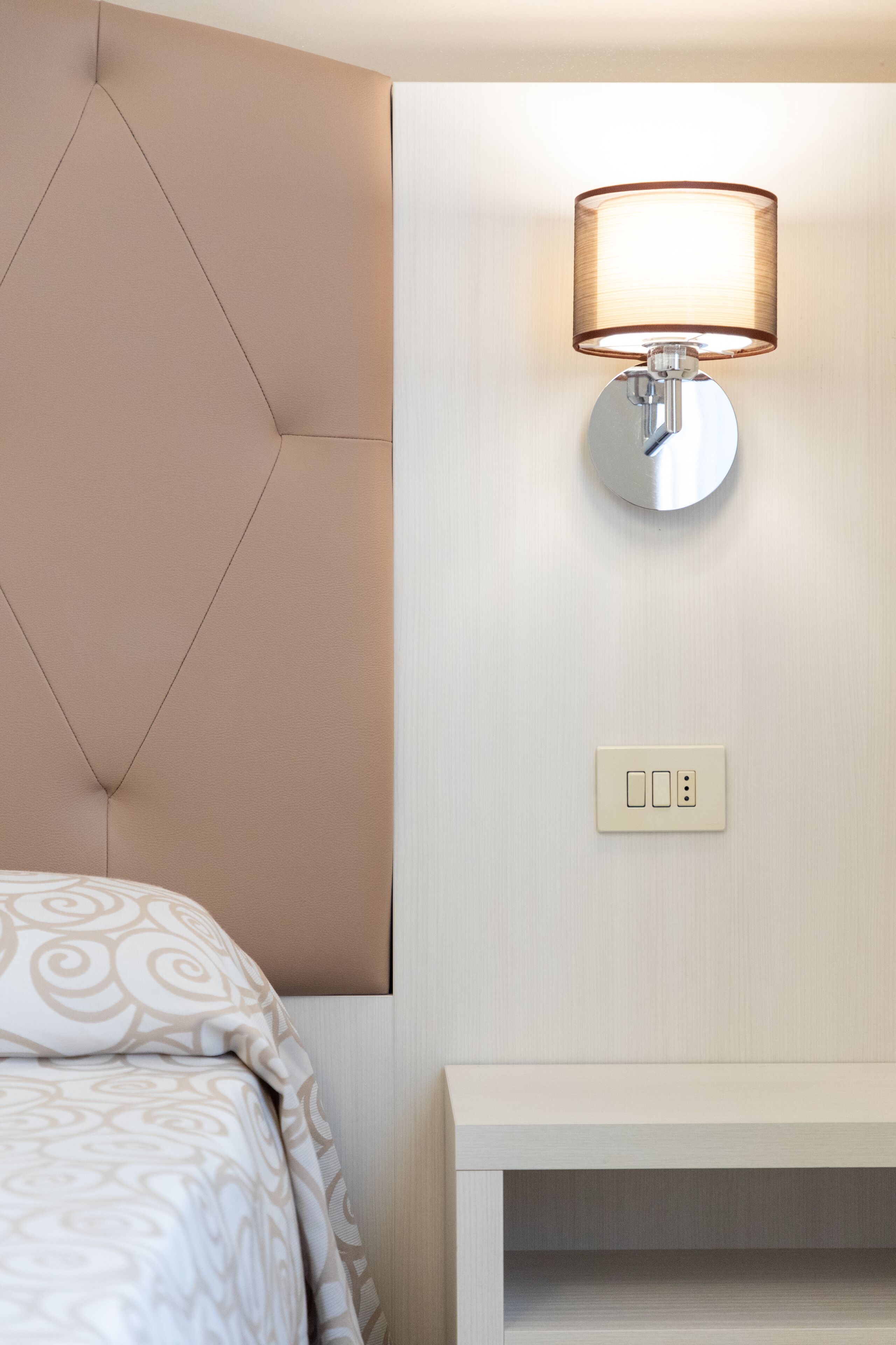 A modern bedroom with a tufted headboard, a bedside table, and a wall-mounted lamp.