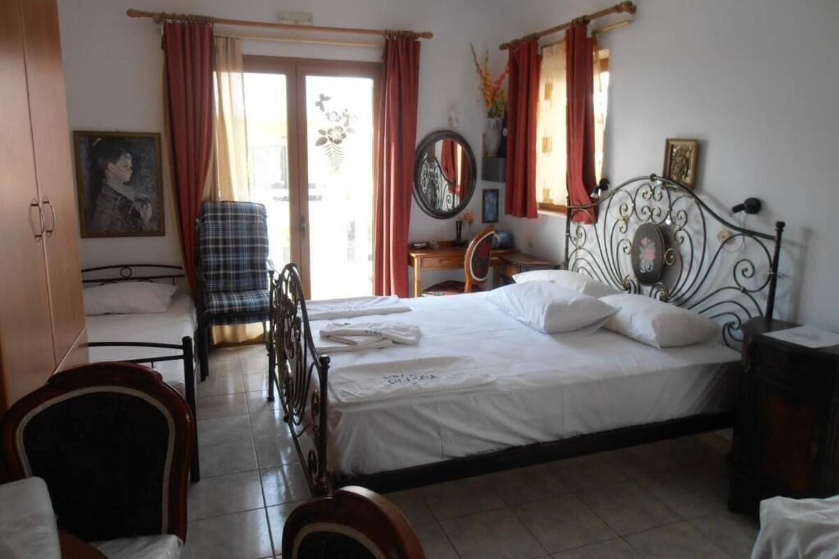 A bedroom with a bed, a chair, a desk, and a window with curtains.