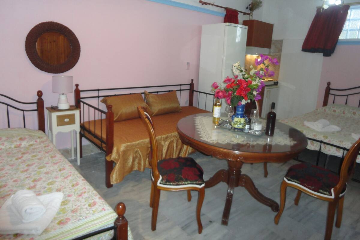 A room with a bed, a round table with chairs, a small cabinet, and a mirror on the wall.