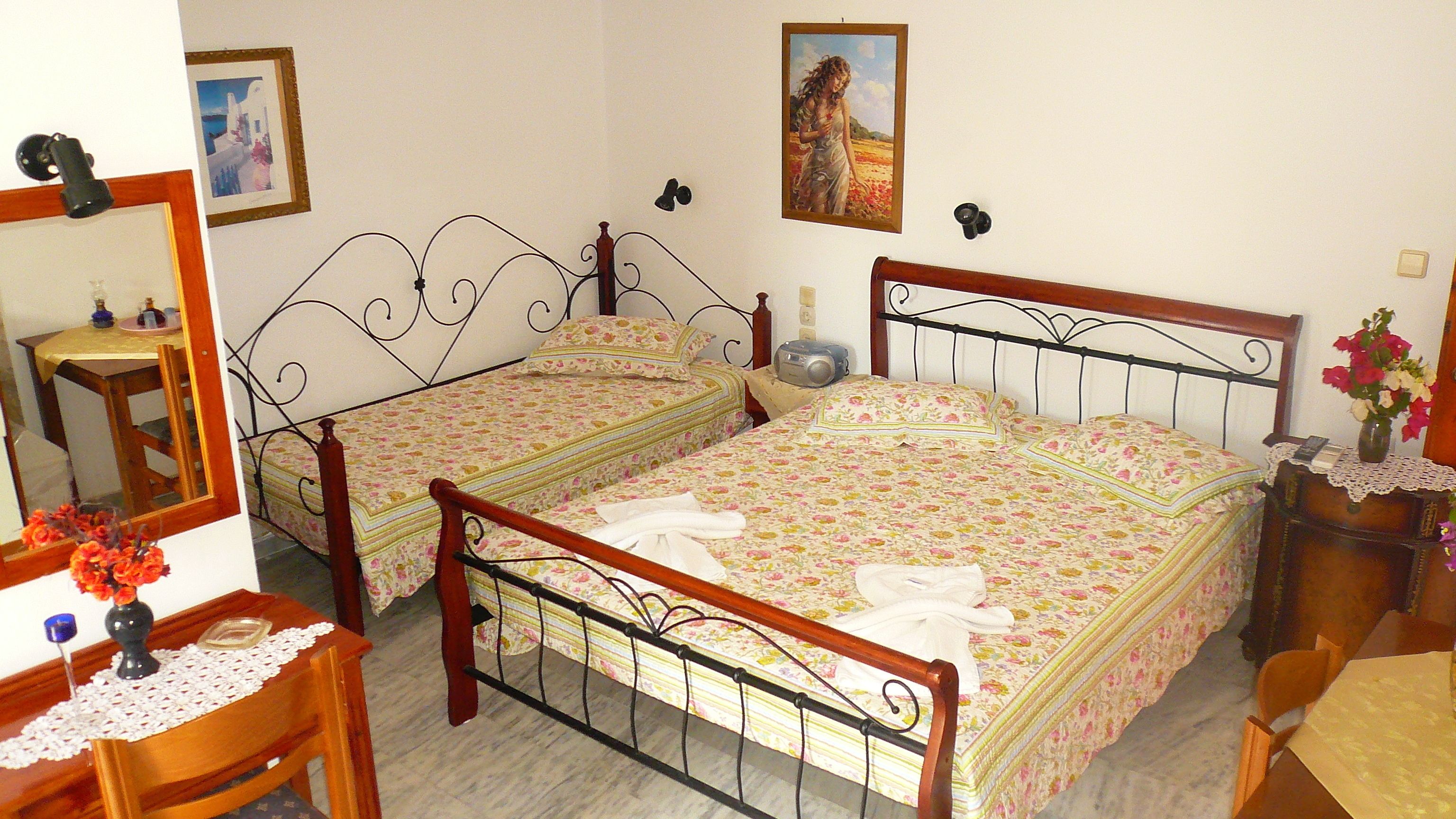 Quarto com duas camas de solteiro, cômoda de madeira, escrivaninha com cadeira, espelho e quadro pendurado na parede.