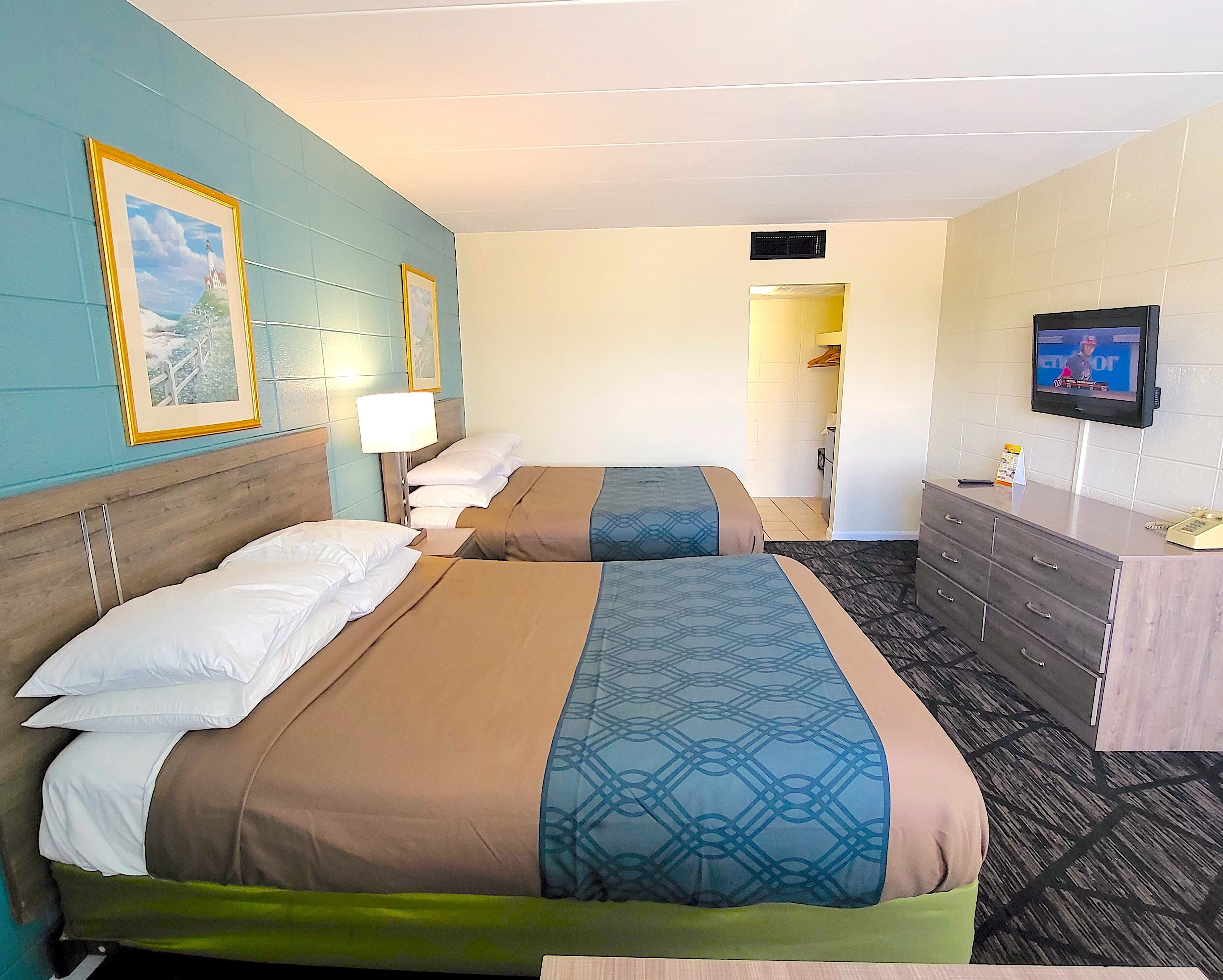 A hotel room with two beds, a dresser, a television, and framed pictures on the wall.