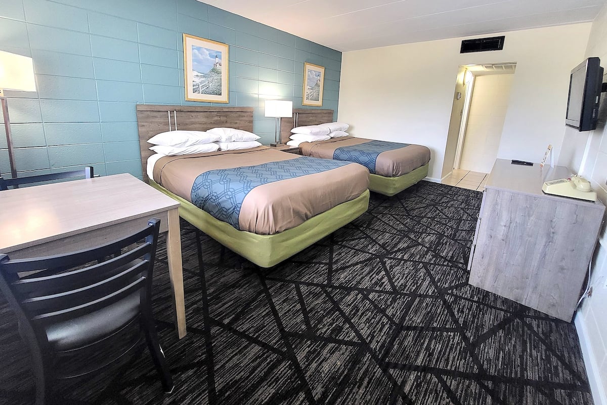 Ein Hotelzimmer mit zwei Betten, einem Schreibtisch, einem Stuhl, einem Fernseher und einem Badezimmer.