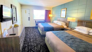 Habitación de hotel con dos camas, un escritorio, televisión y ventana con cortinas.