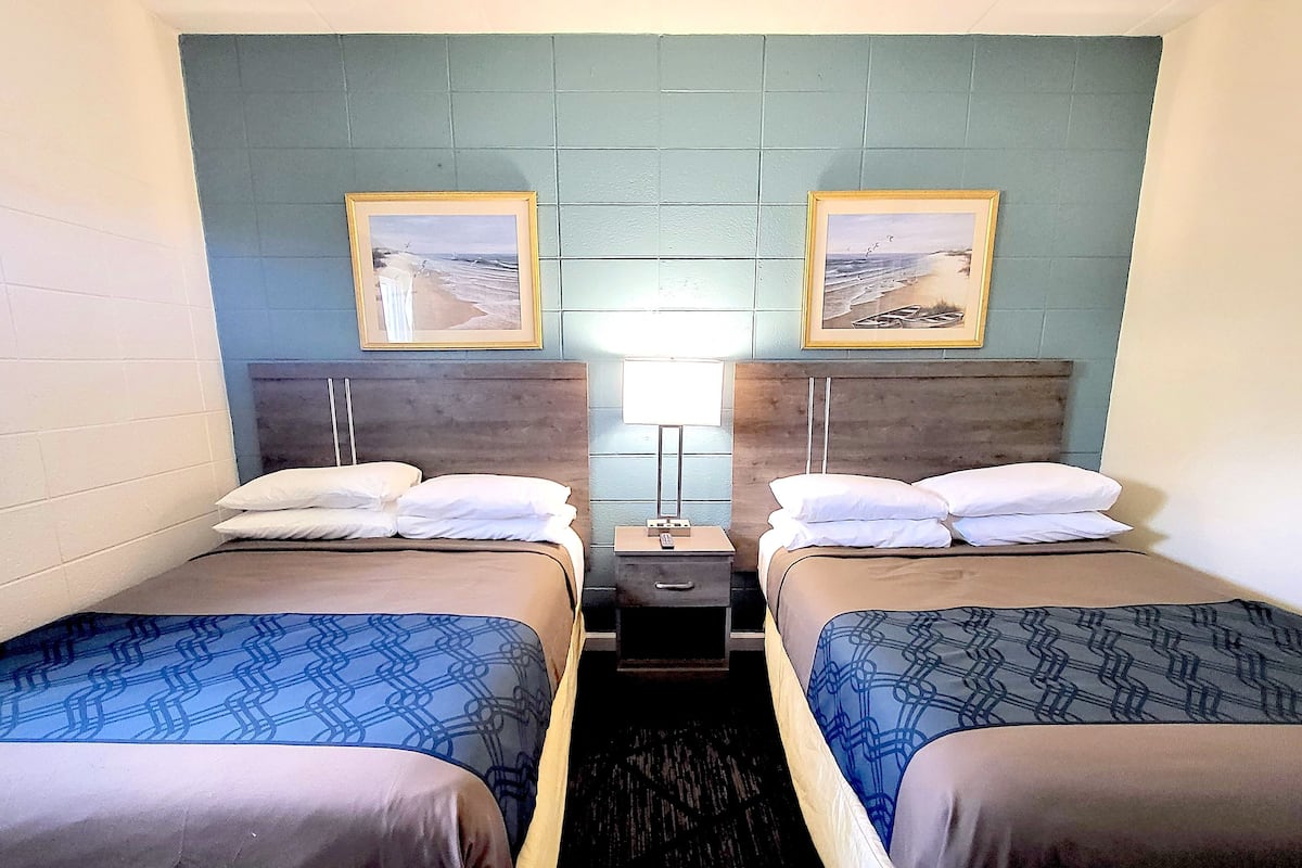 Ein Hotelzimmer mit zwei Einzelbetten, einem Nachttisch mit Lampe sowie zwei gerahmten Bildern an der Wand.