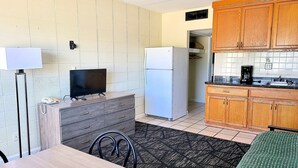 Una cocina compacta con refrigerador, microondas y armarios de madera. Cuenta con un comedor con mesa y sillas.