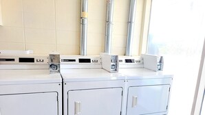 Una sala de lavandería con varias lavadoras y secadoras, un panel de control y una ventana que proporciona luz natural.