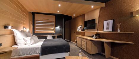 A modern hotel room with a bed, a desk, a sofa, and a small kitchen area.