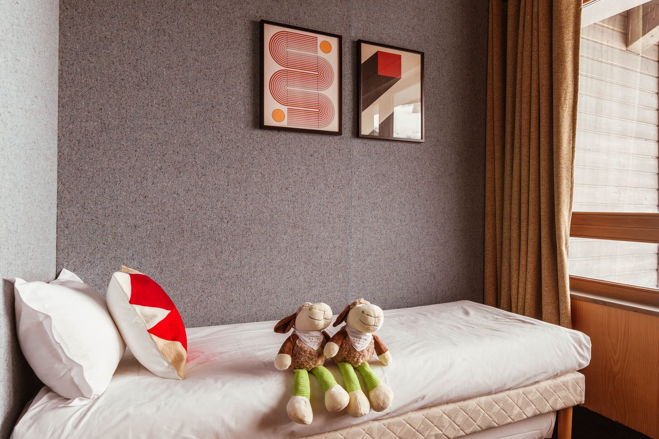 A hotel room with a bed, two plush toys, a pillow, and two framed artworks on the wall.