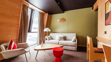 Ein modernes Wohnzimmer mit einer Couch, einem roten Hocker, einem Holztisch und einem Fenster mit Vorhängen.