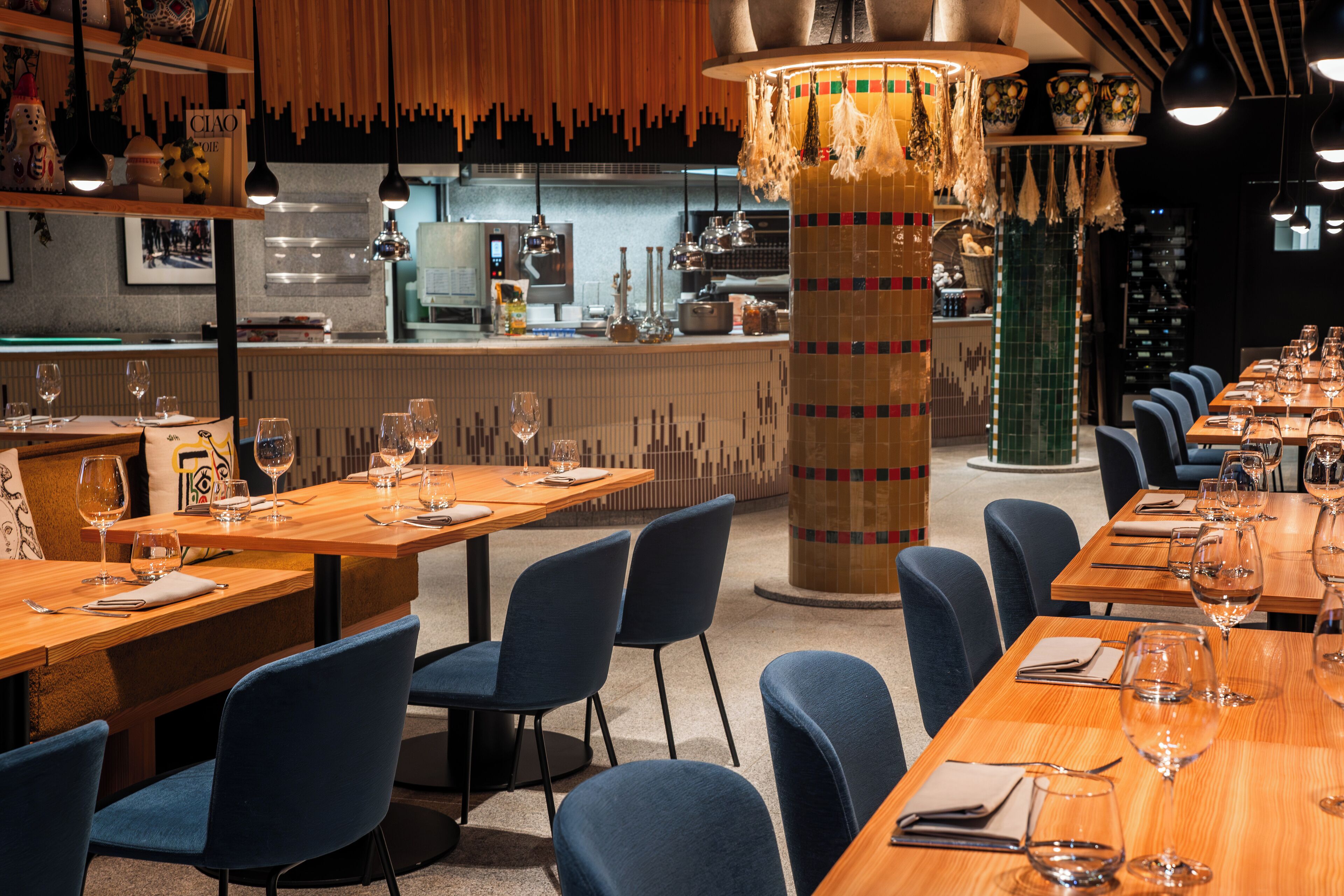 Un restaurante con varias mesas y sillas, una zona de bar y un pilar decorativo.