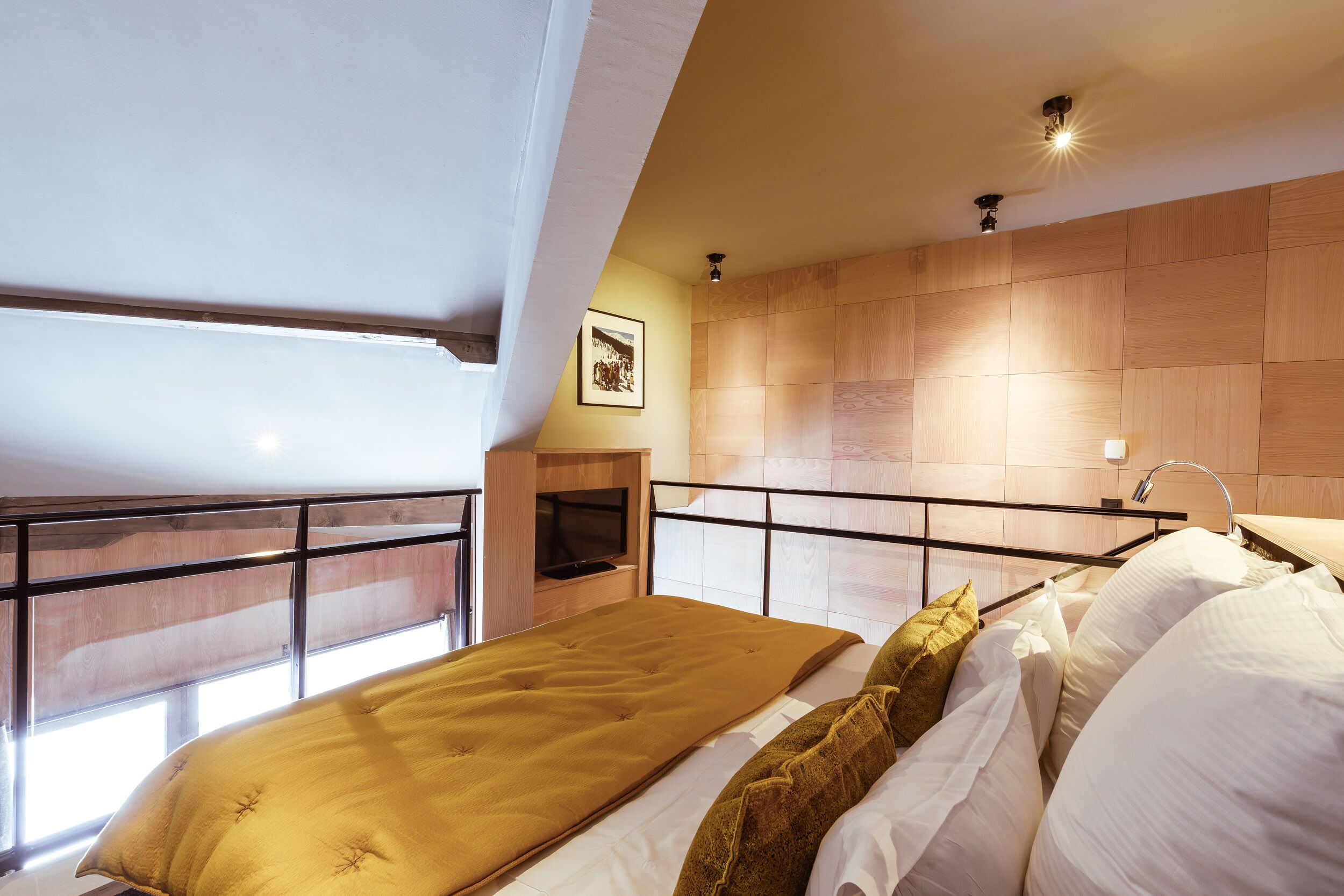 A bedroom with a bed, a window, a mounted TV, and a wooden wall.