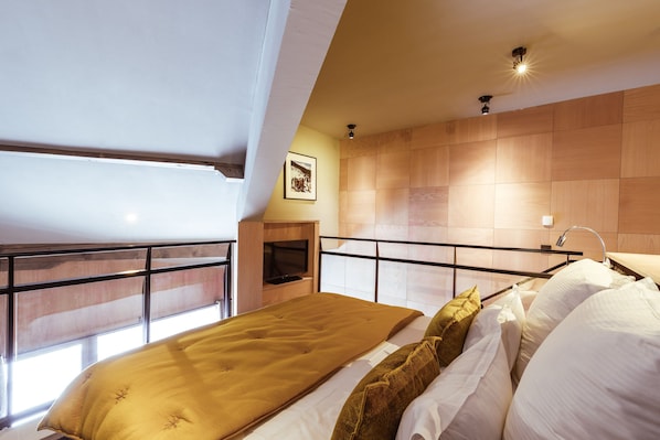 A bedroom with a bed, a window, a mounted TV, and a wooden wall.
