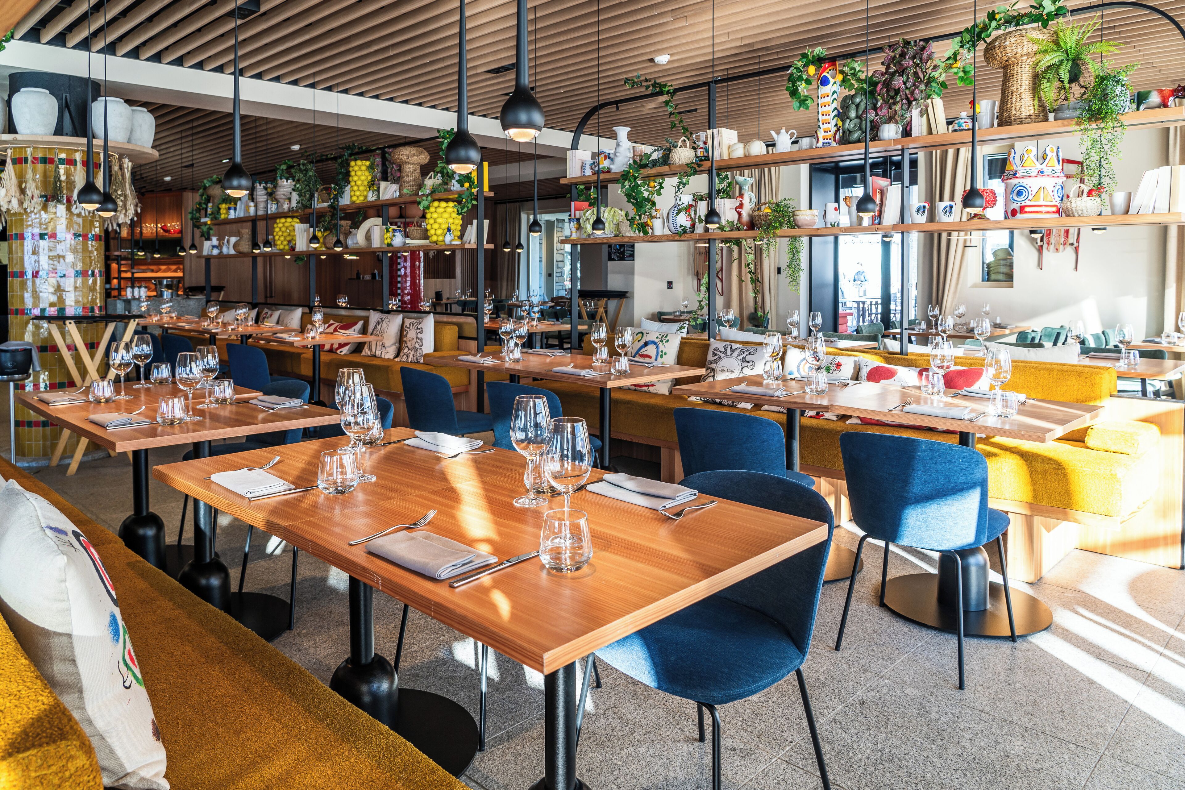 A restaurant with multiple dining tables, blue chairs, and a variety of decorative items on shelves.