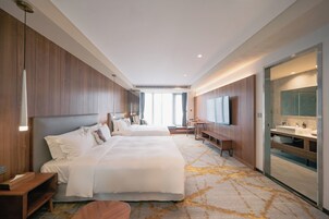 A modern hotel room with a large bed, a desk, a television, and a bathroom with a mirror and sink.