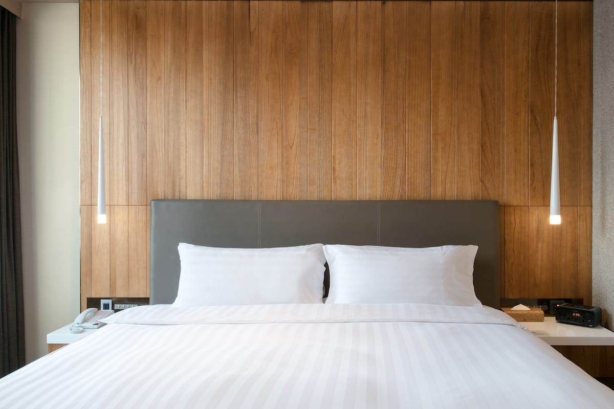 Une chambre d’hôtel avec un grand lit, un mur lambrissé en bois et une table de chevet équipée d’un téléphone et d’un réveil.