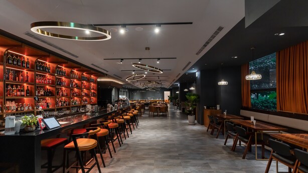 A bar area with a long counter, multiple stools, and a variety of bottles and glasses on shelves. - Home Hotel (Taipei)