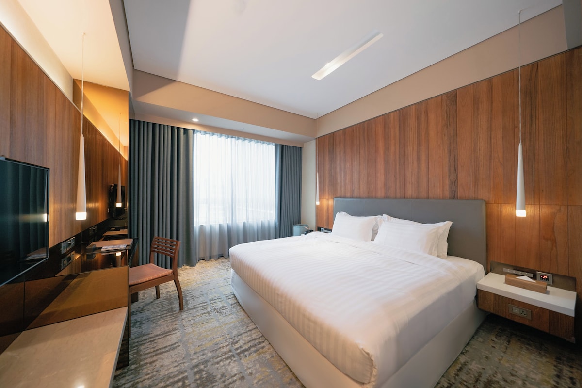 A hotel room with a large bed, a desk with a chair, a television, and a window with curtains.