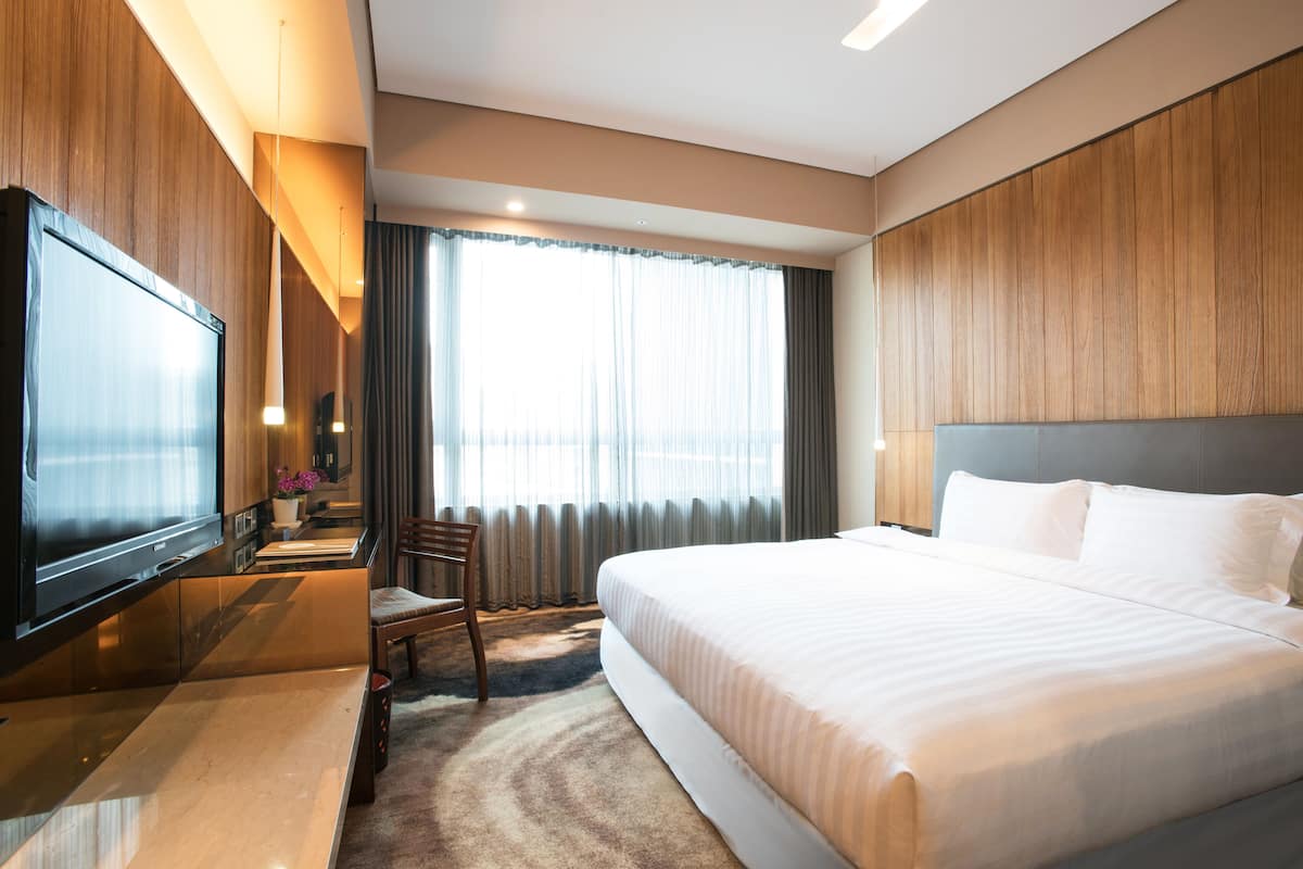 Une chambre d’hôtel avec un grand lit, un téléviseur à écran plat, un bureau avec une chaise et une fenêtre avec des rideaux.
