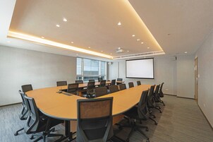 Een vergaderzaal met een grote ovale tafel, meerdere stoelen, een projectiescherm en een groot raam.