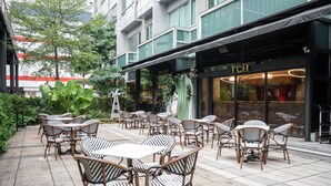 An outdoor patio with wicker tables and chairs, a building with a 'RENT' sign, and a green awning. - Home Hotel (Taipei)