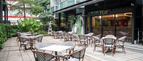 An outdoor patio with wicker tables and chairs, a building with a 'RENT' sign, and a green awning.