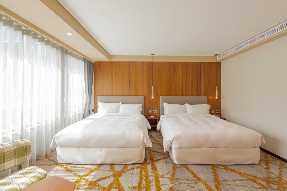 Une chambre d’hôtel avec deux lits, un canapé et une grande fenêtre avec des rideaux légers.