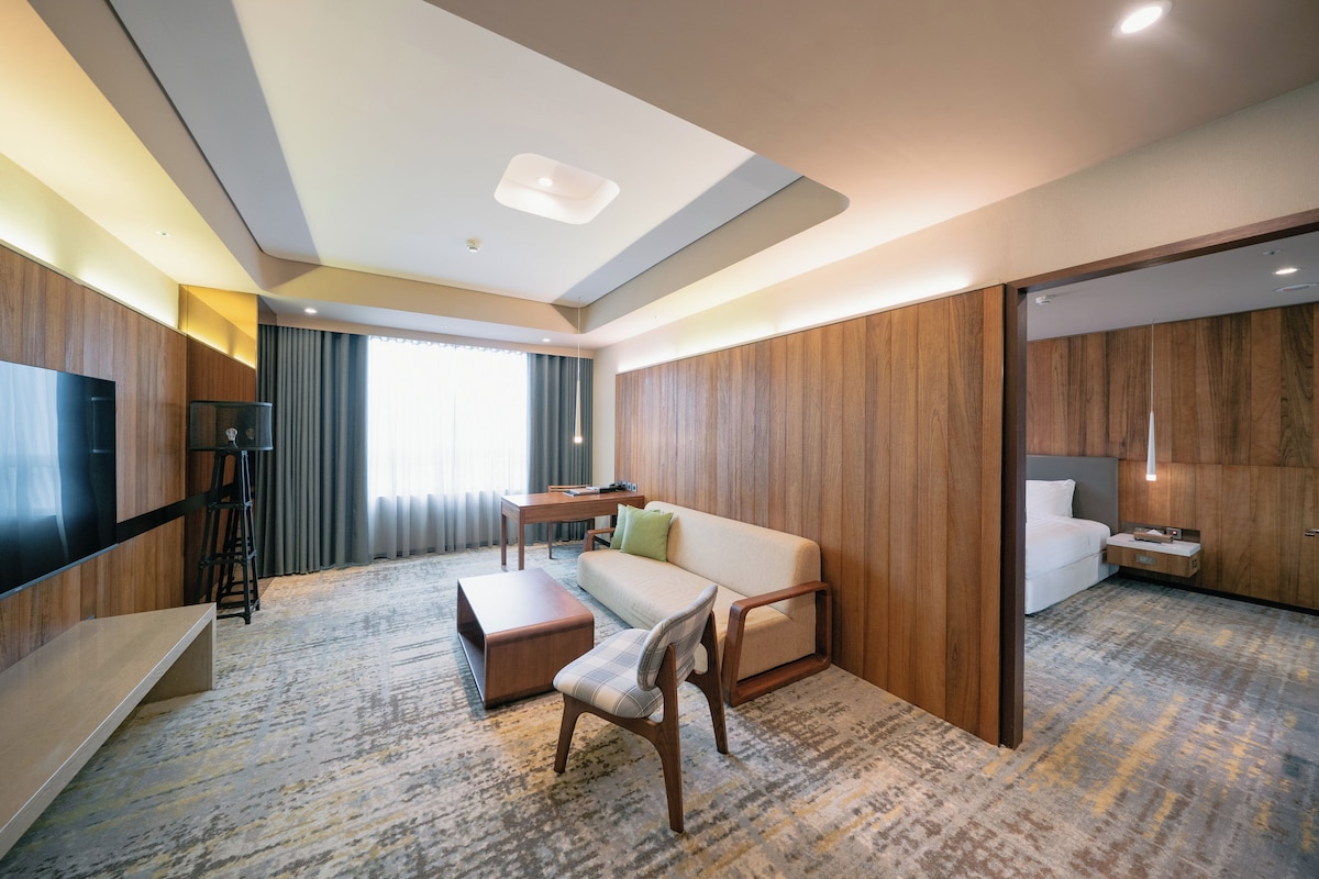 A hotel room with a sofa, a dining table, a TV, and a desk.