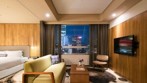 A modern hotel room with a large bed, a sofa, a coffee table, and a TV. The room has a view of a cityscape at night. - Home Hotel (Taipei)