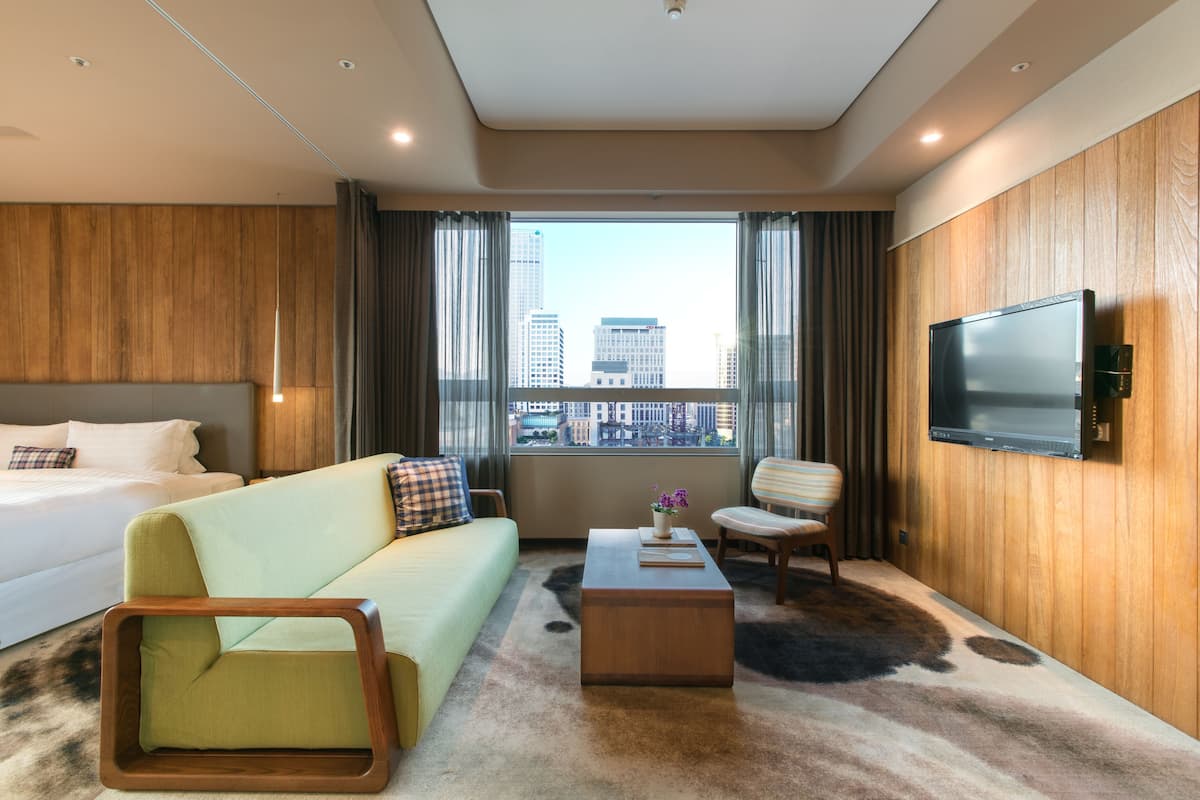 Une chambre d’hôtel moderne équipée d’un lit, d’un canapé, d’un fauteuil, d’une table basse et d’un téléviseur fixé au mur.