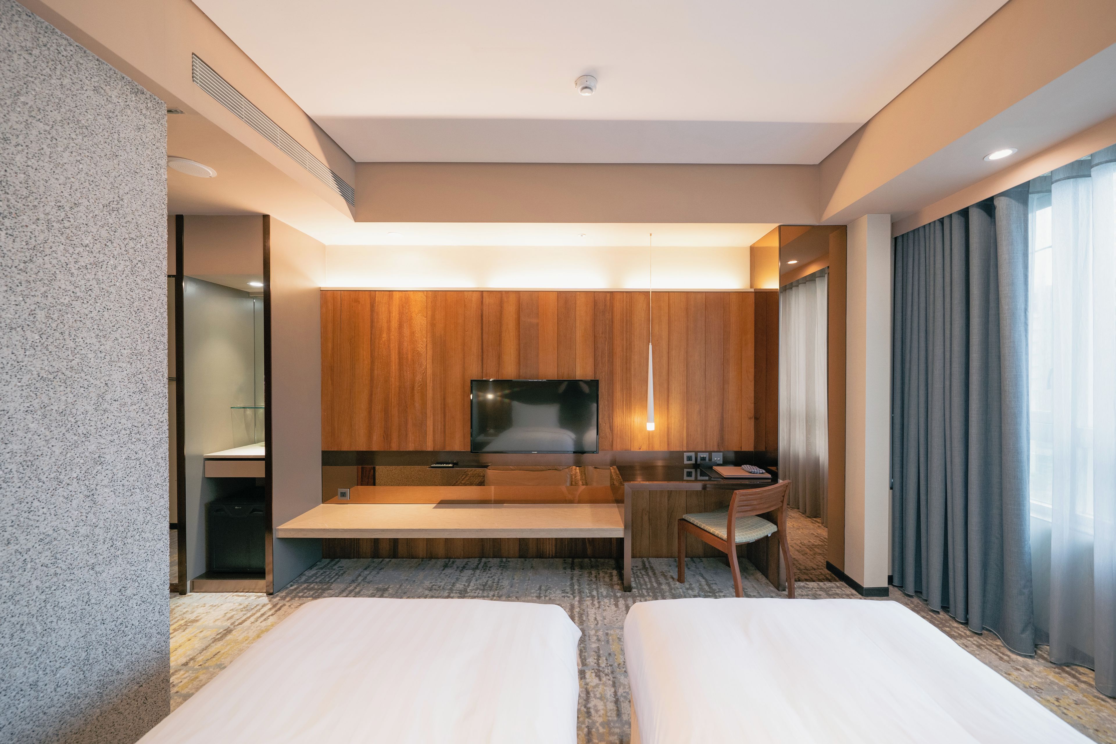 A hotel room with a bed, a desk, a chair, a television, and a large window with curtains.
