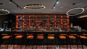 A bar area with multiple shelves of bottles, a long counter, and several bar stools. - Home Hotel (Taipei)