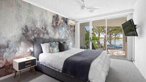 Une chambre à coucher moderne avec un grand lit, une table de chevet, un ventilateur de plafond et un téléviseur fixé au mur.