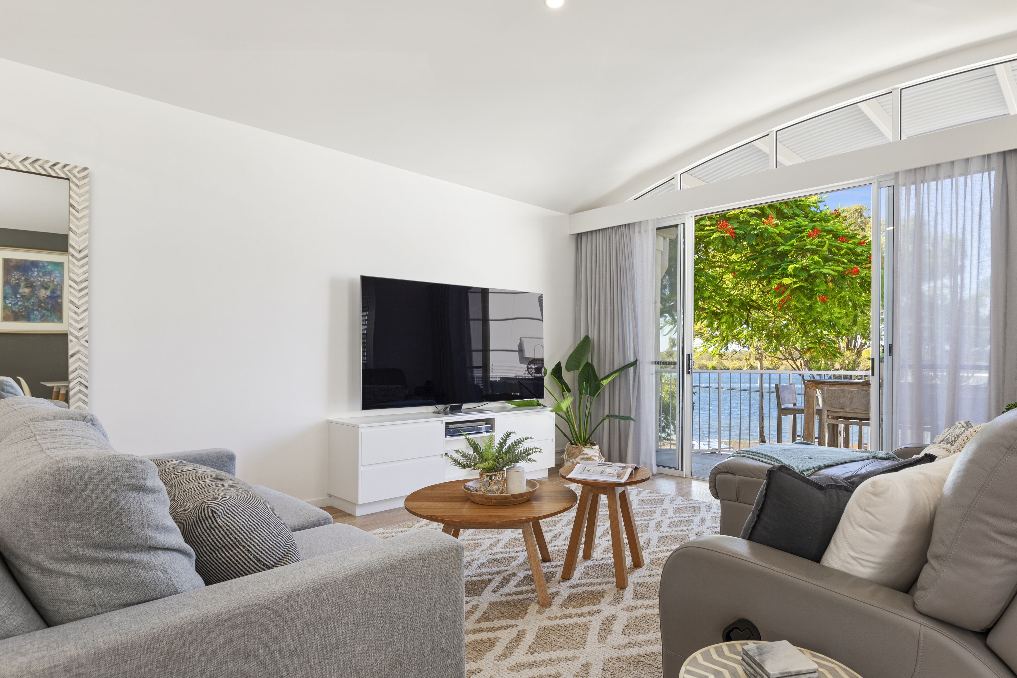 Een moderne woonkamer met een flatscreen televisie, een bank, een salontafel en een balkon met uitzicht op groen en een zwembad.