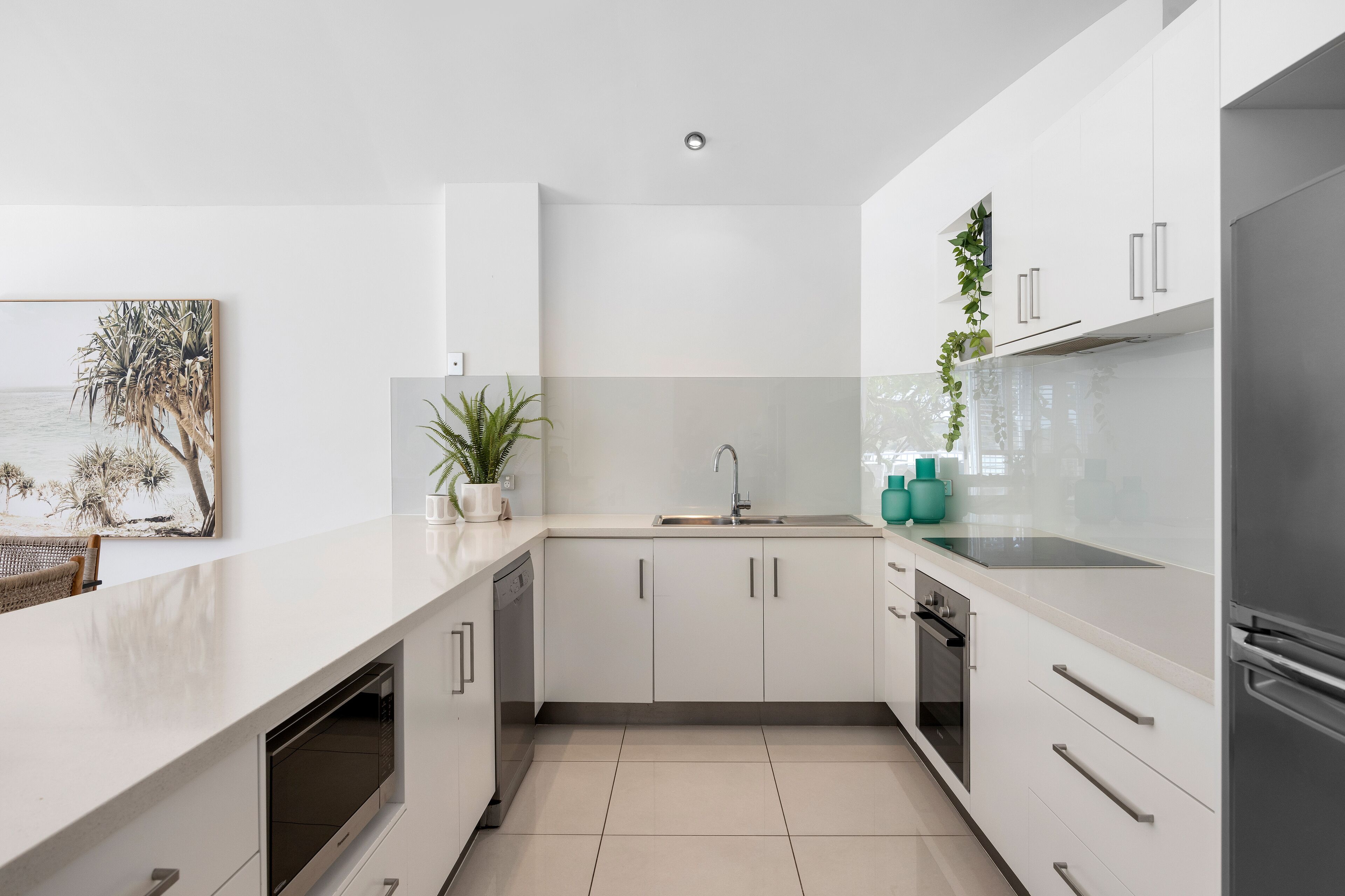 A modern kitchen with white cabinetry, a stainless steel sink, and a built-in oven.