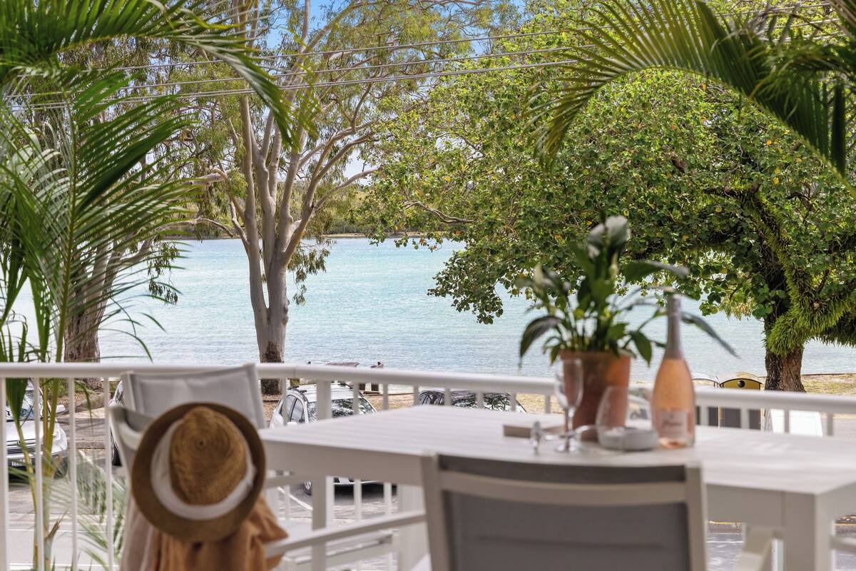 Une terrasse offrant une vue sur la mer, entourée d’une végétation luxuriante et agrémentée de mobilier blanc.