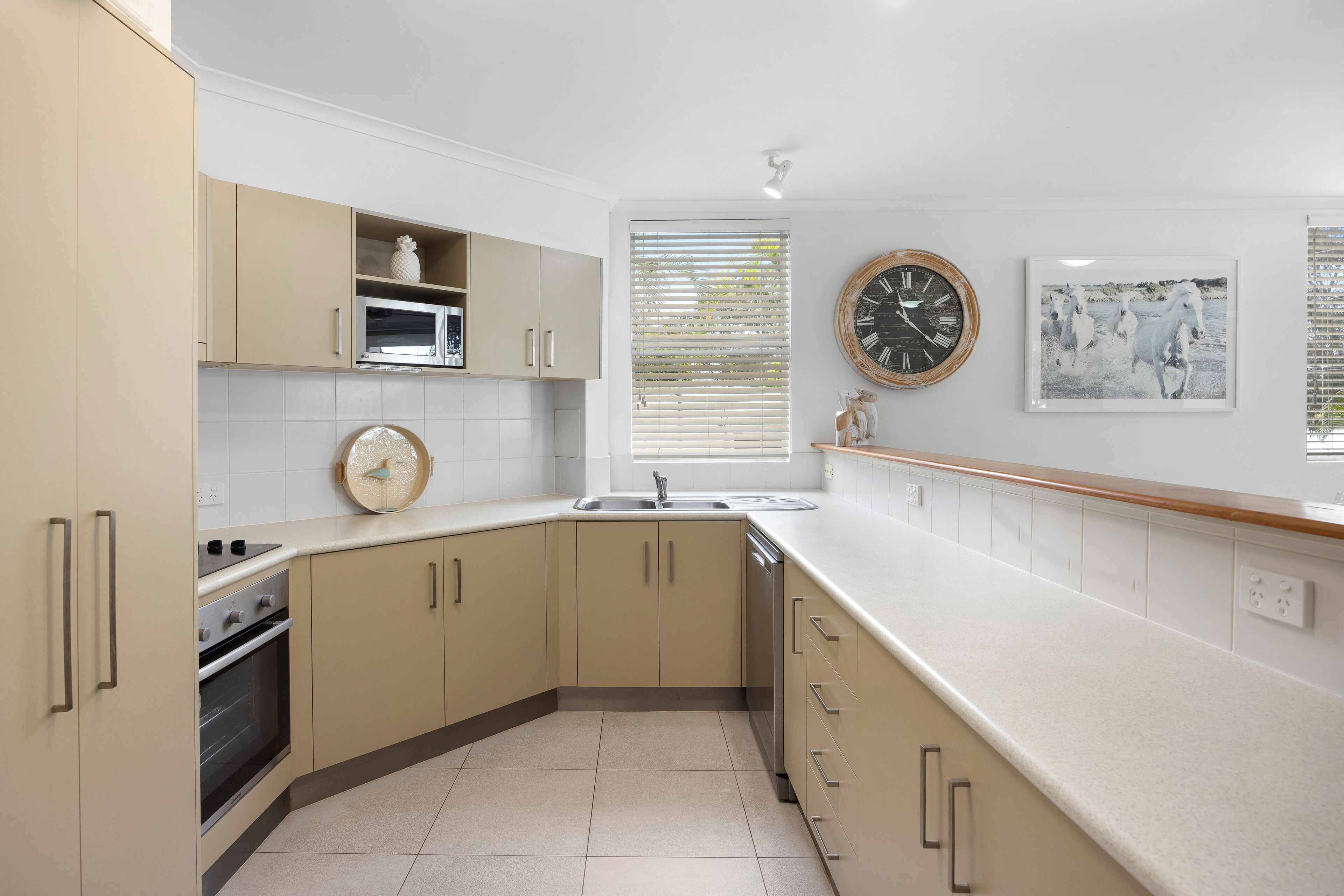 Una cocina con armarios color beige, una encimera blanca, un reloj y un cuadro en la pared.