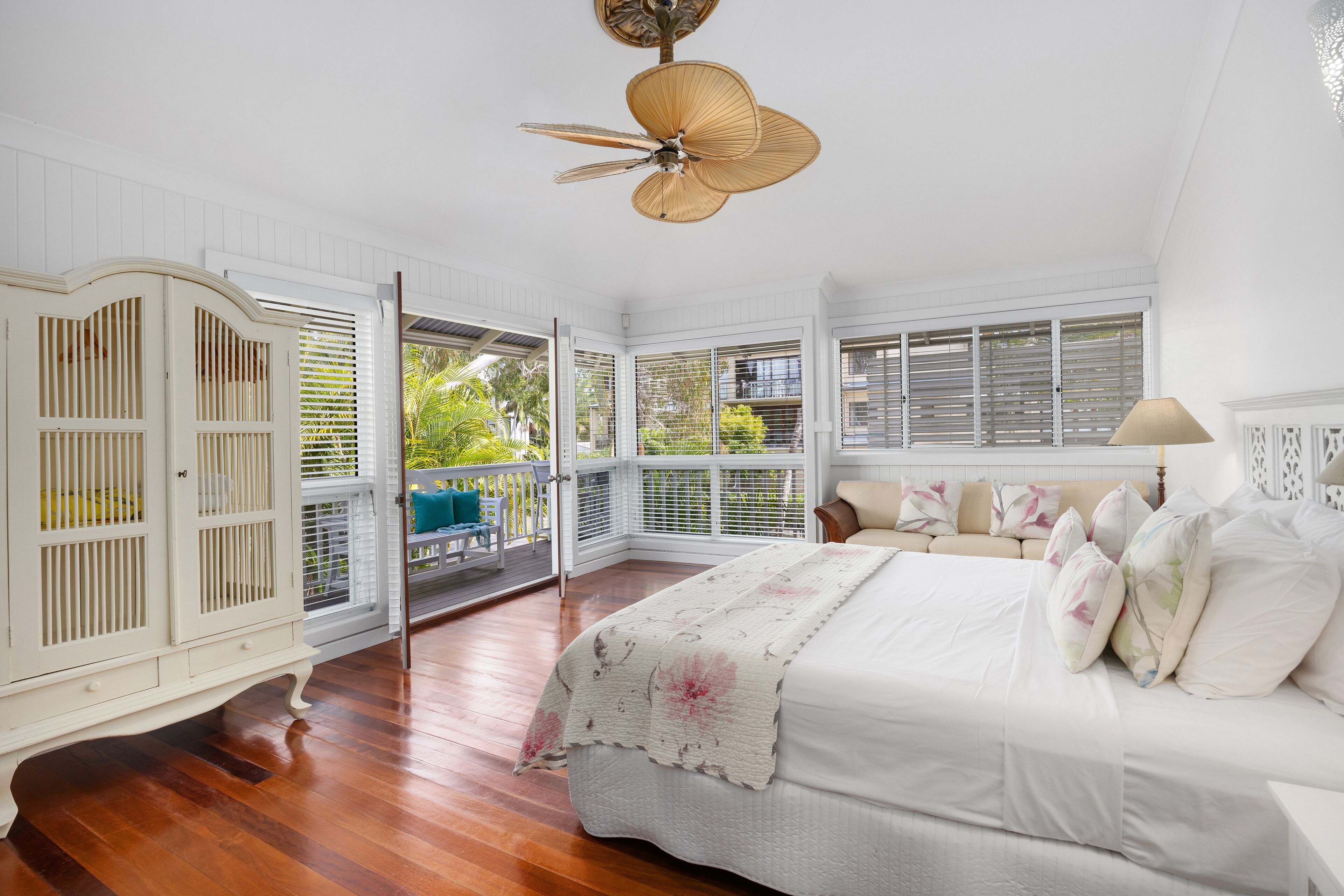 A bedroom with a large bed, a ceiling fan, and a view of the outdoors.