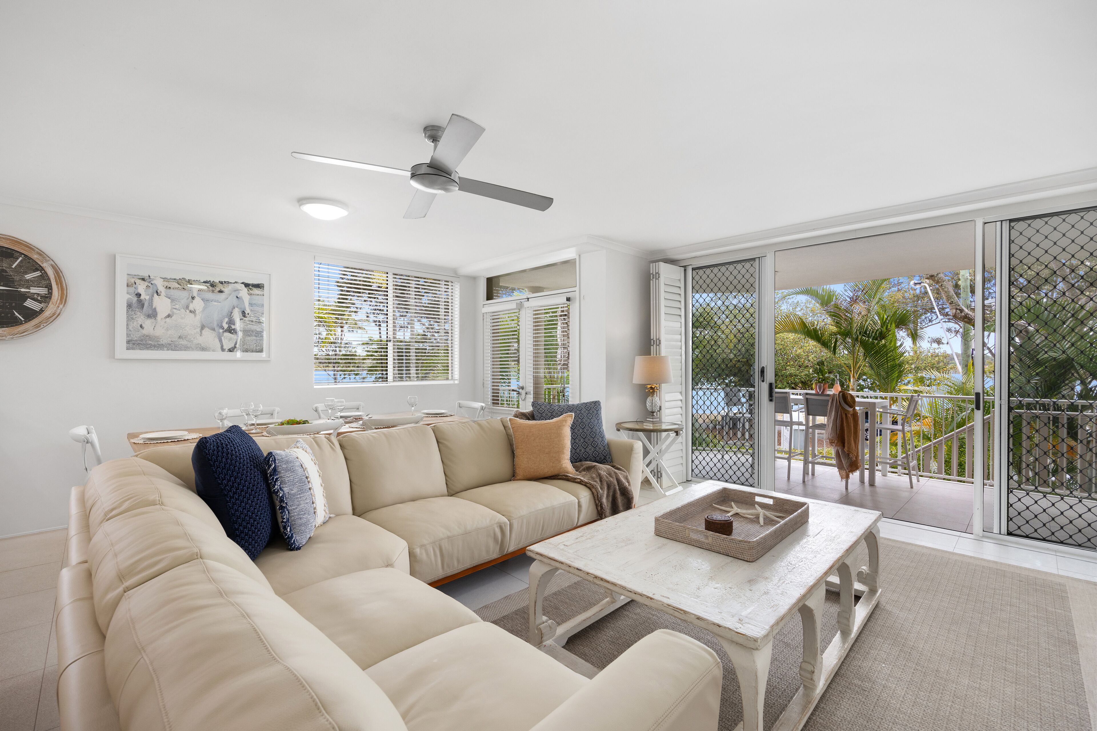 A living room with a beige sectional sofa, a white coffee table, and a ceiling fan.