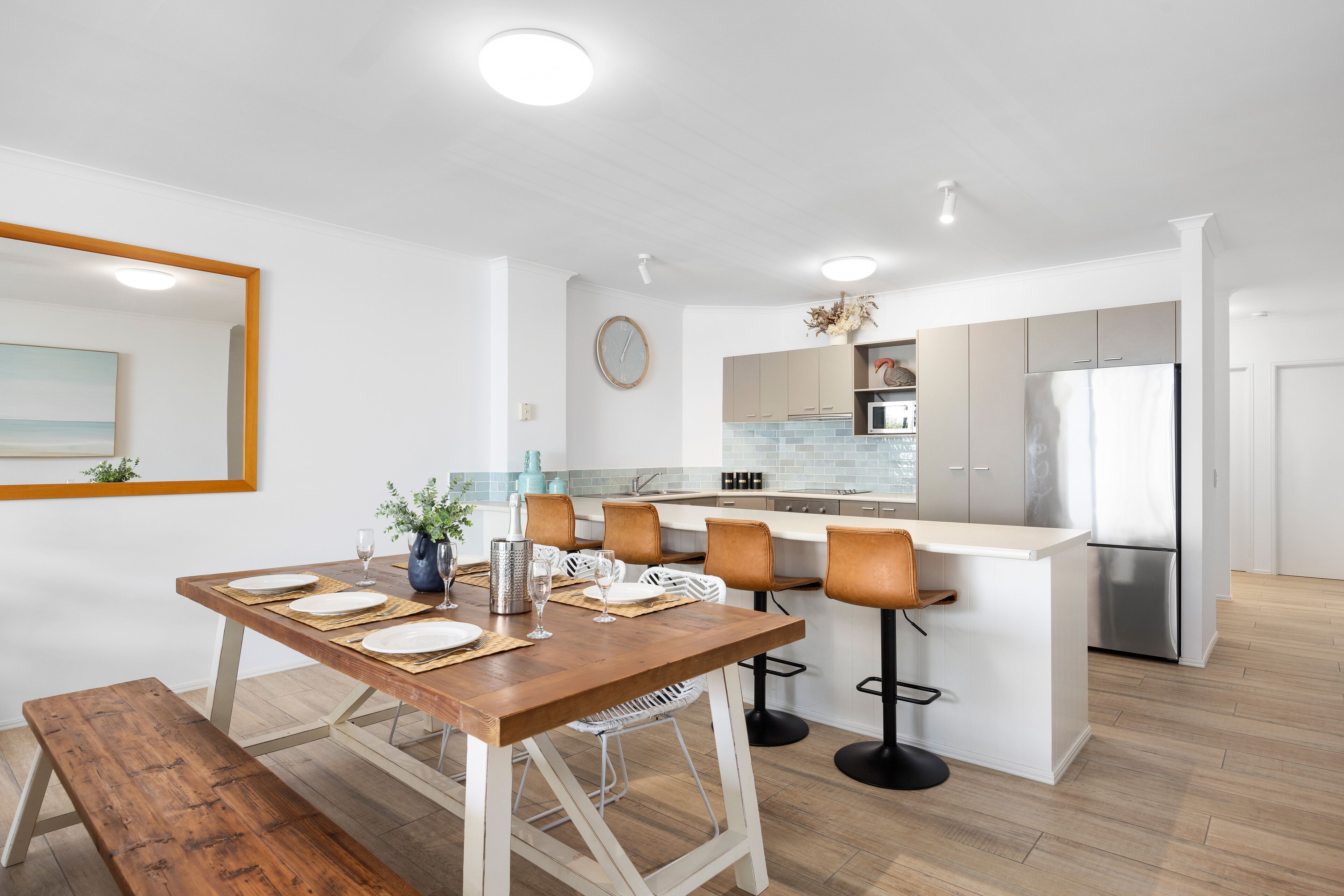 Eine moderne Küche mit weißen Schränken, einem Edelstahlkühlschrank und einem Essbereich mit Holztisch und -stühlen.