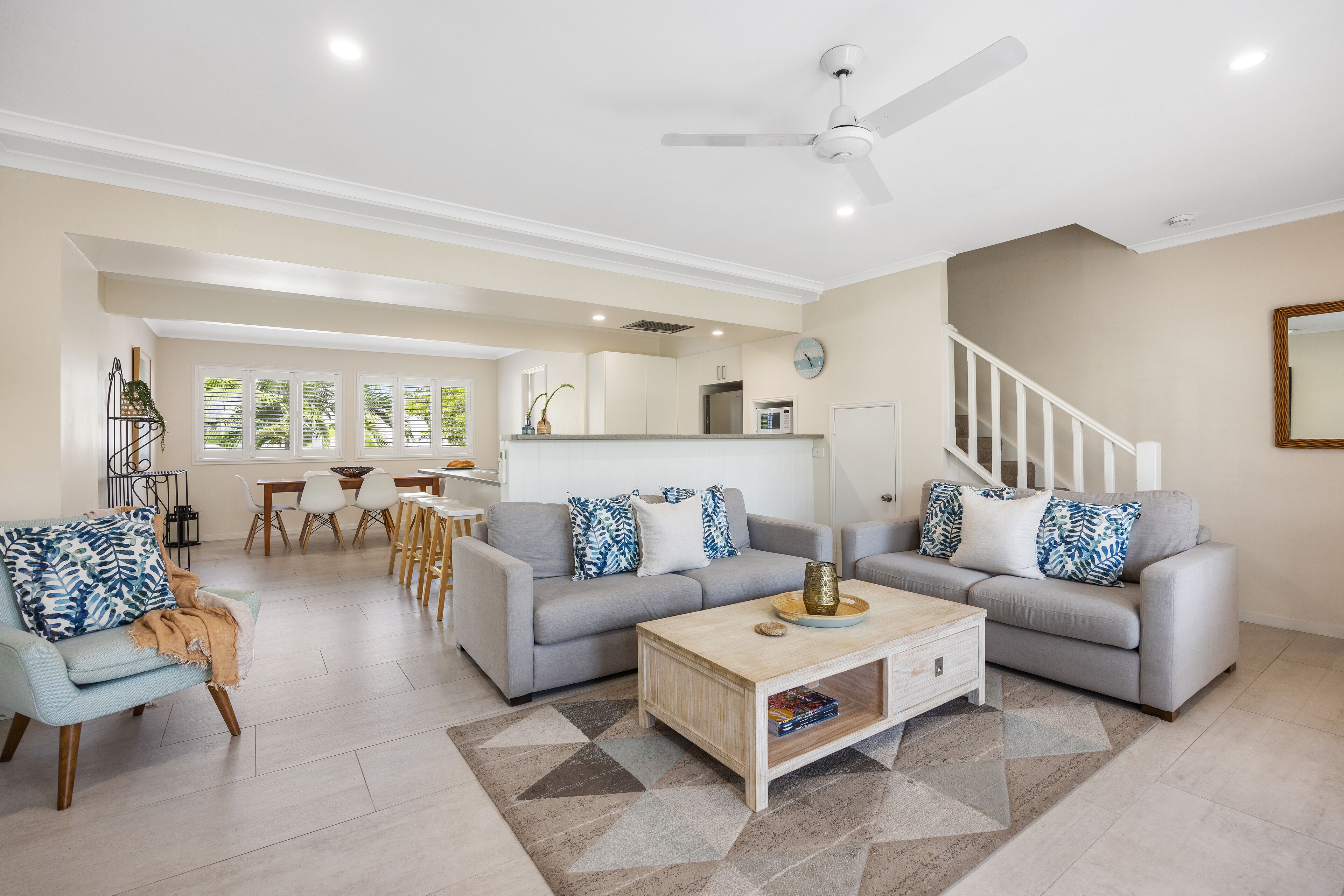 A spacious living room with a grey sofa, a coffee table, and a dining area with a white table and chairs.