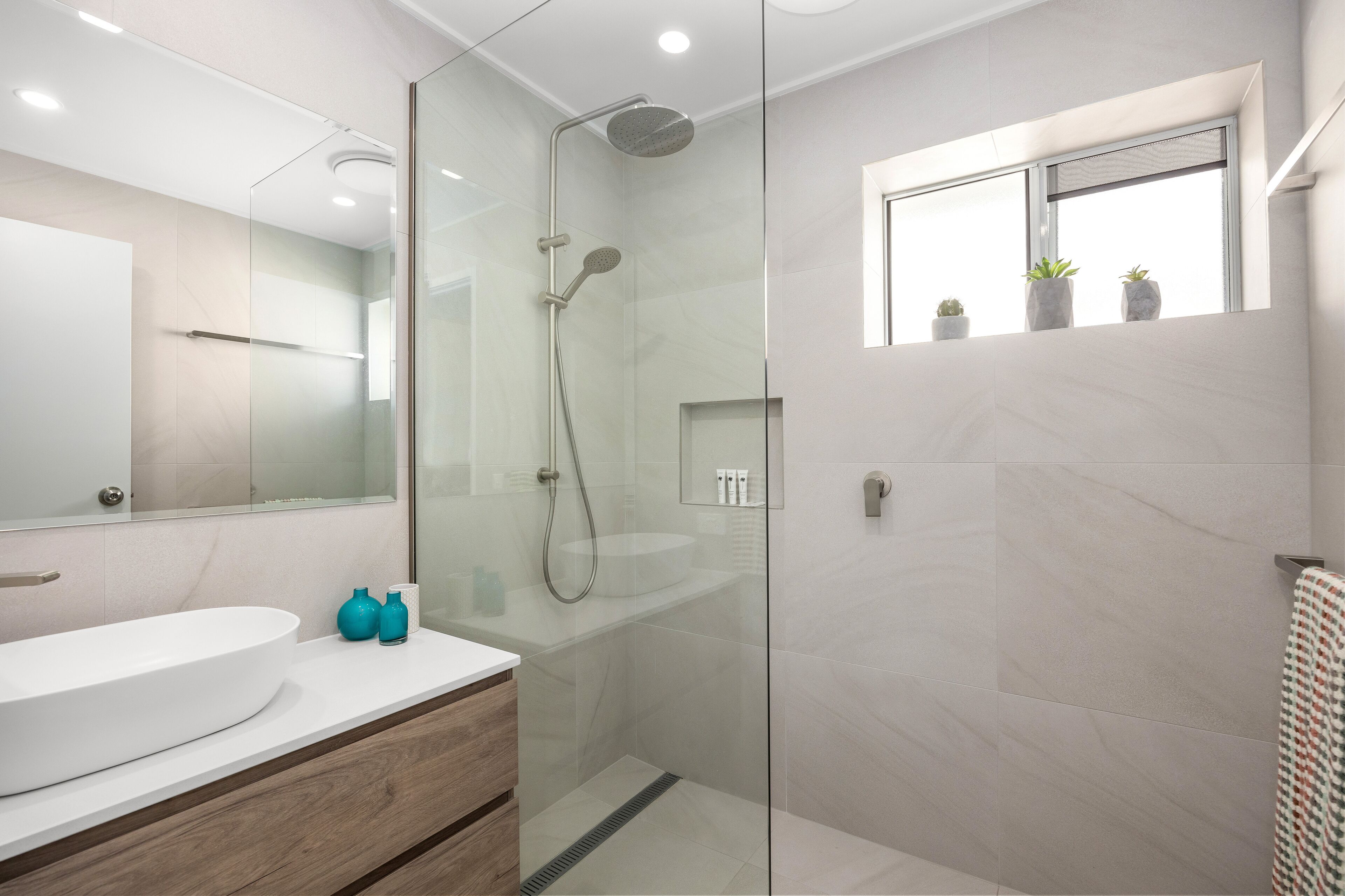 A modern bathroom with a glass-enclosed shower, a white sink, and a window with plants.