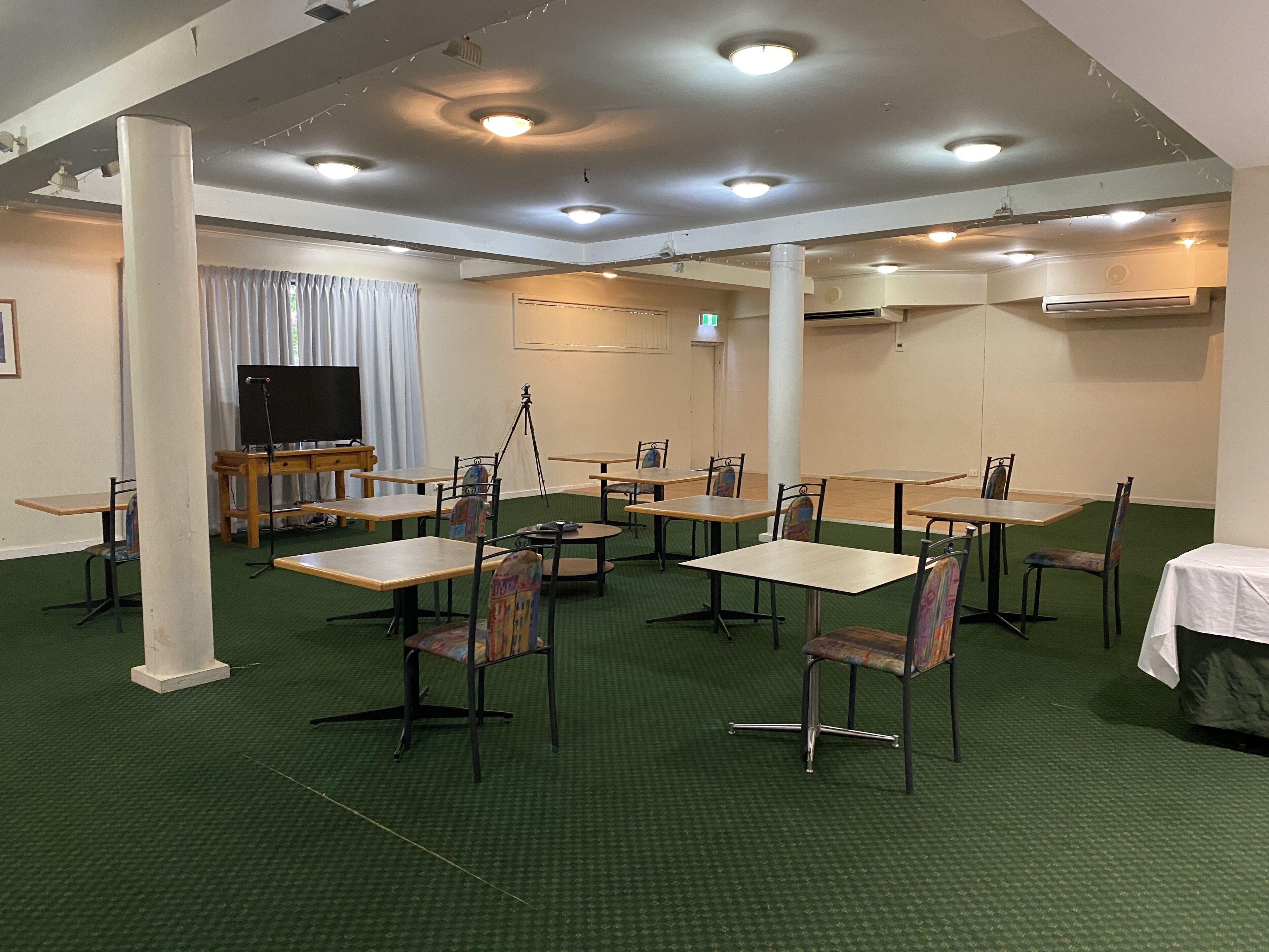 A conference room with green carpet, multiple tables and chairs, a projector, and a television.