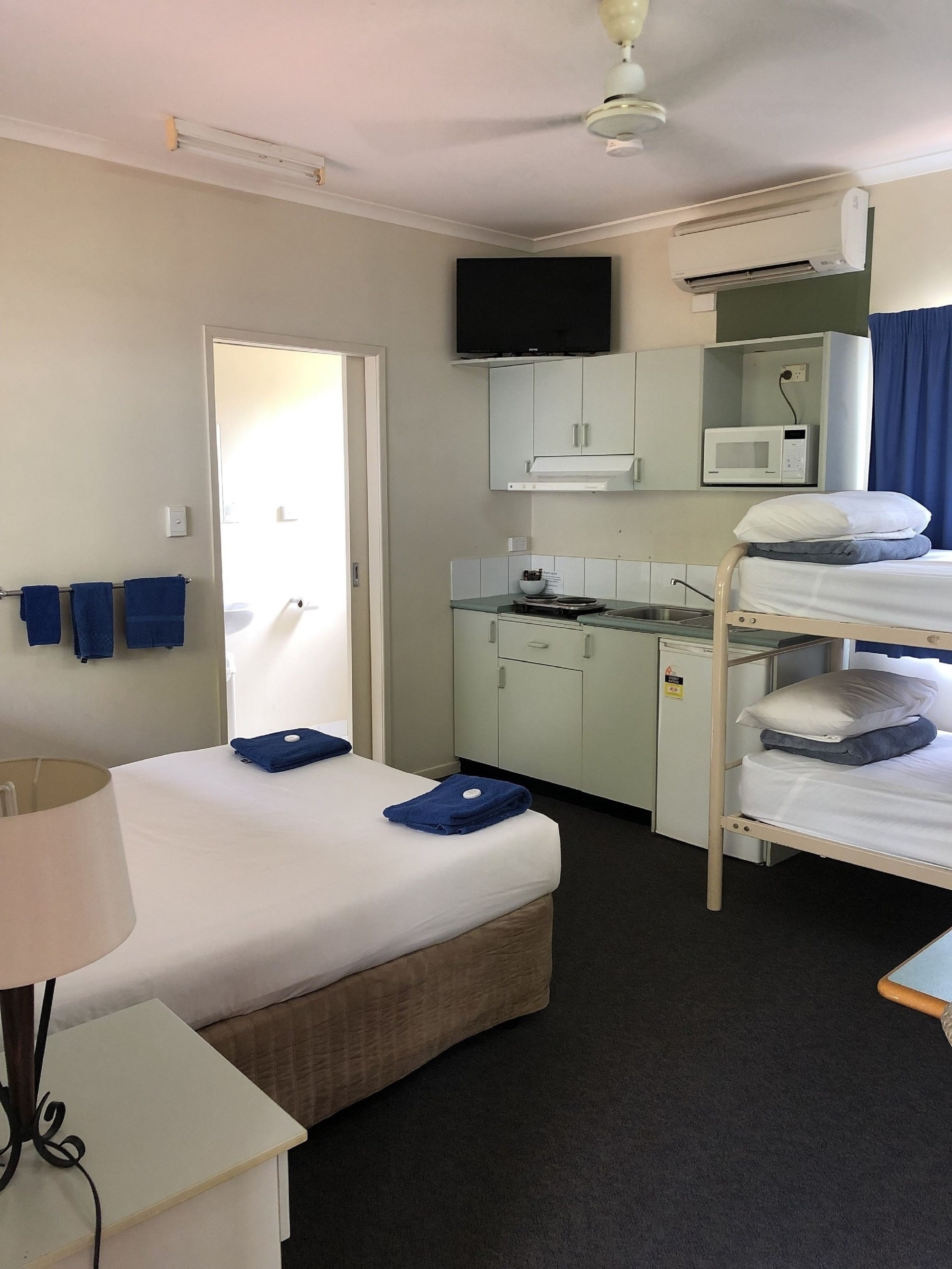 Une chambre d’hôtel compacte comprenant un lit superposé, un bureau avec un micro-ondes, une télévision et une petite kitchenette.