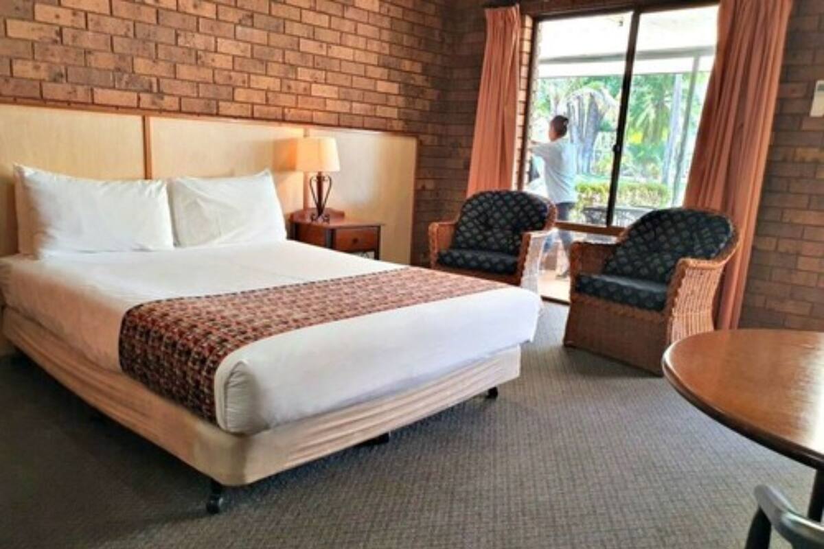 A hotel room with a large bed, a desk, two chairs, a lamp, and a view of the outdoors.