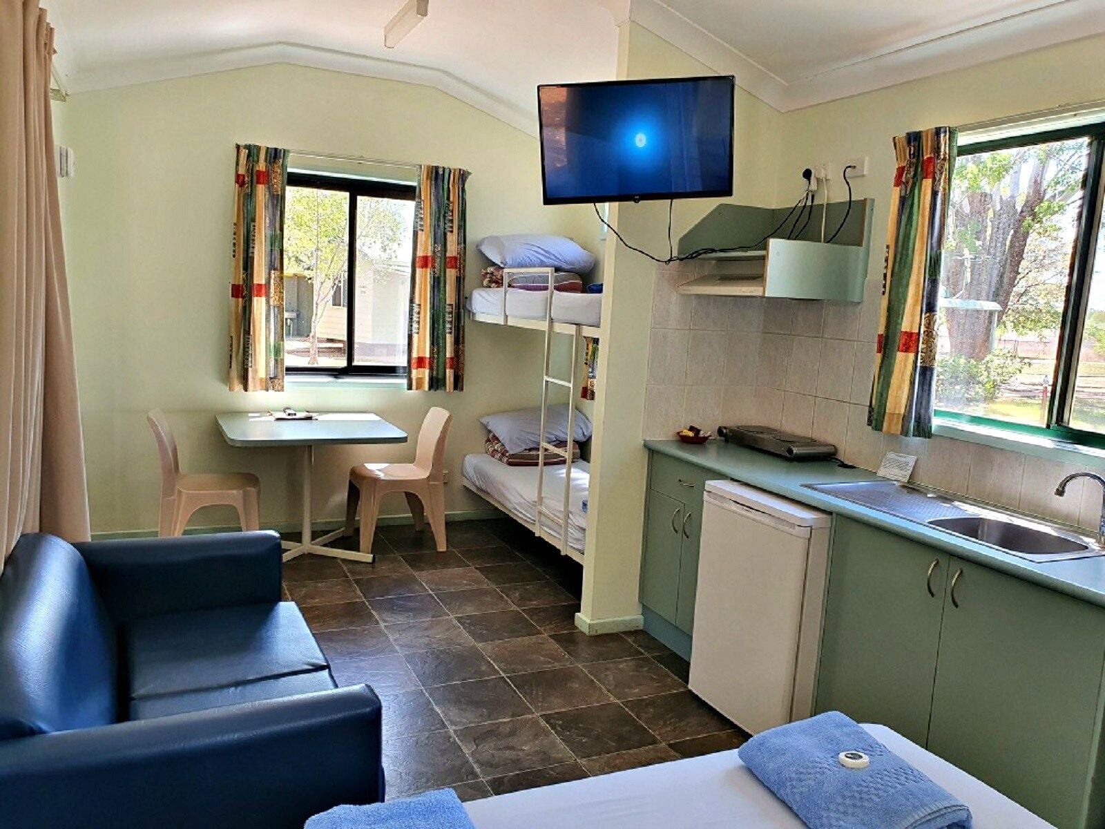 A compact room with bunk beds, a desk, a chair, a television, a sink, and a window with curtains.