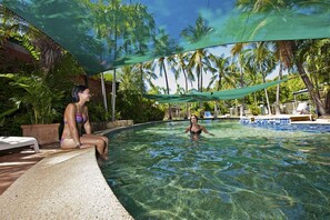 A swimming pool with clear water, surrounded by palm trees and a shaded area. - Knotts Crossing Resort (Katherine)