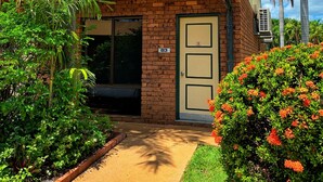 A small brick building with a door labeled "83", surrounded by lush greenery and palm trees. - Knotts Crossing Resort (Katherine)